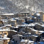 Panorama di Aosta in primavera, con fiori che sbocciano e montagne innevate sullo sfondo.